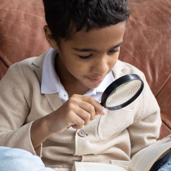 Child with dark skin and short black hair looks at an item in a magnifying glass