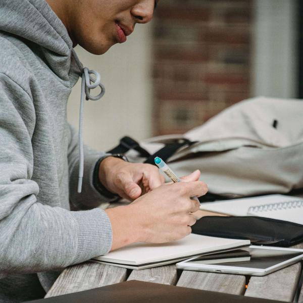Torso of a young adult in a grey hoodie writing on a picnic table