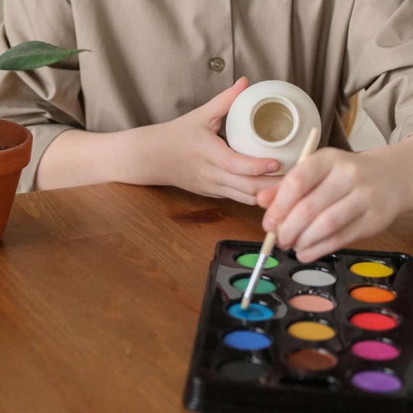 Hands and torso of very light skinned child painting a vase