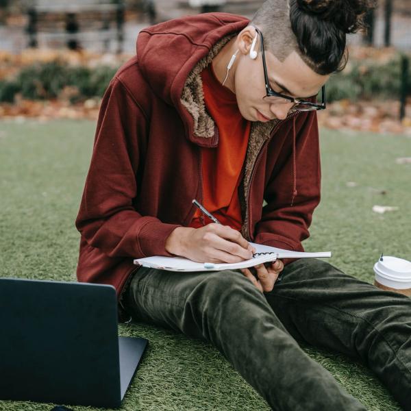 A student writing notes on a notepad in the grass