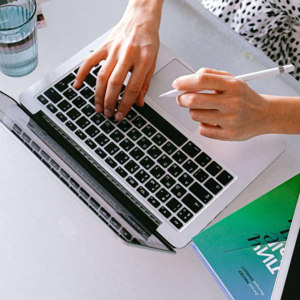 Top rear view of hands at a laptop. An iPad is lying next to the laptop