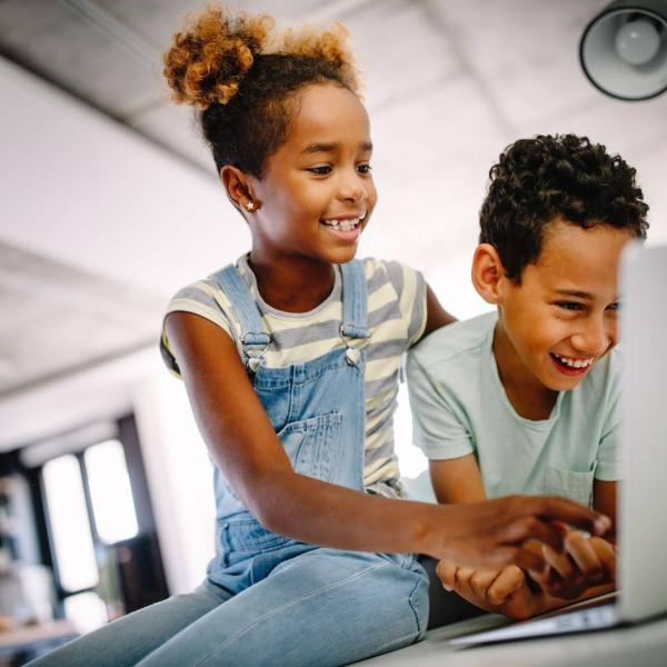 two elementary-aged children looking at a laptop and smiling