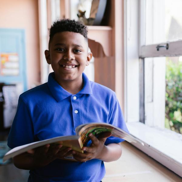 Student smiling with textbook in bedroom