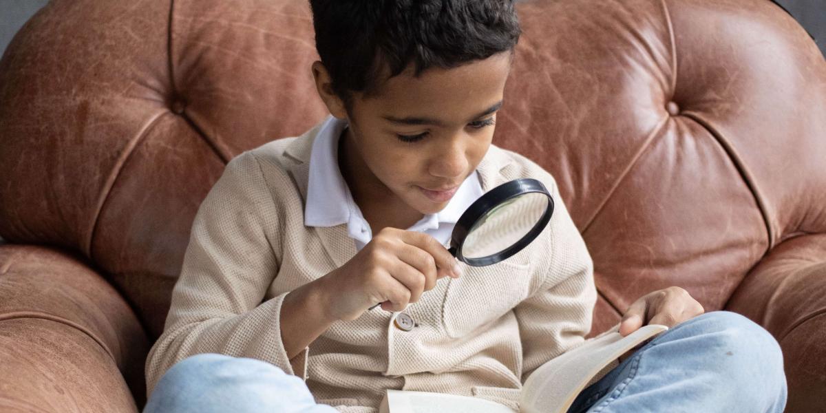 Child with dark skin and short black hair looks at an item in a magnifying glass