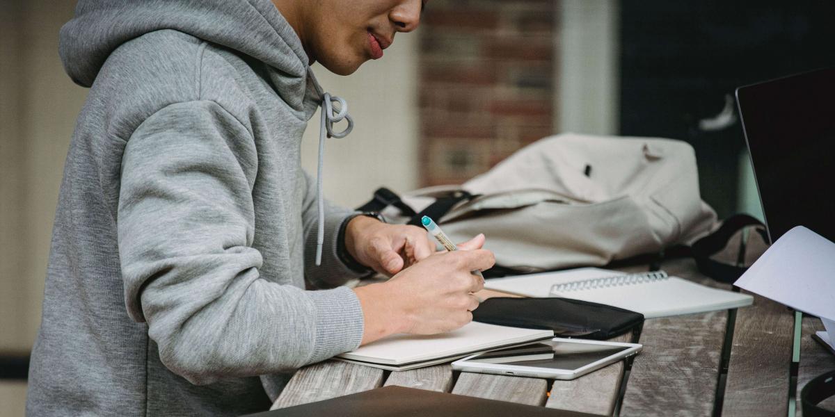 Torso of a young adult in a grey hoodie writing on a picnic table