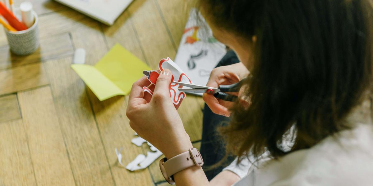 Top view of person with medium-length brown hair cutting out items for a craft project