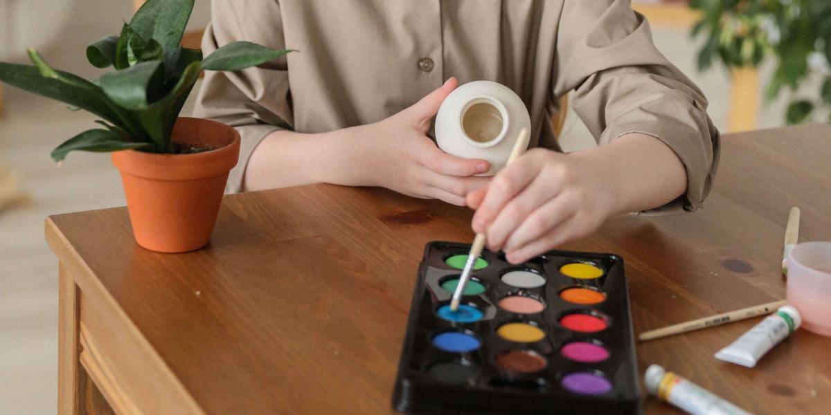 Hands and torso of very light skinned child painting a vase