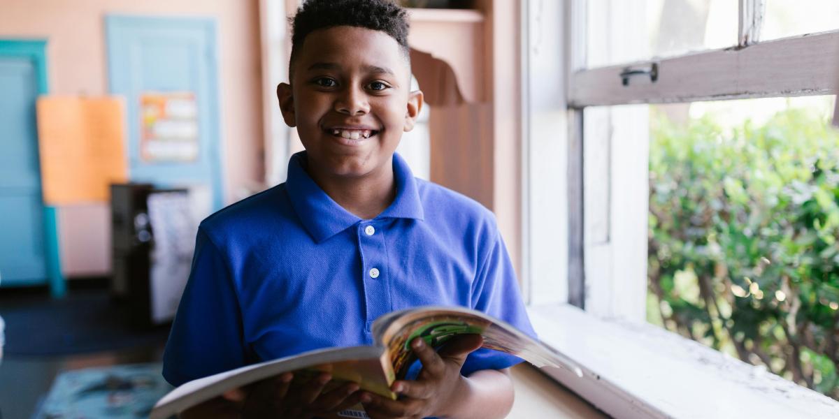 Student smiling with textbook in bedroom