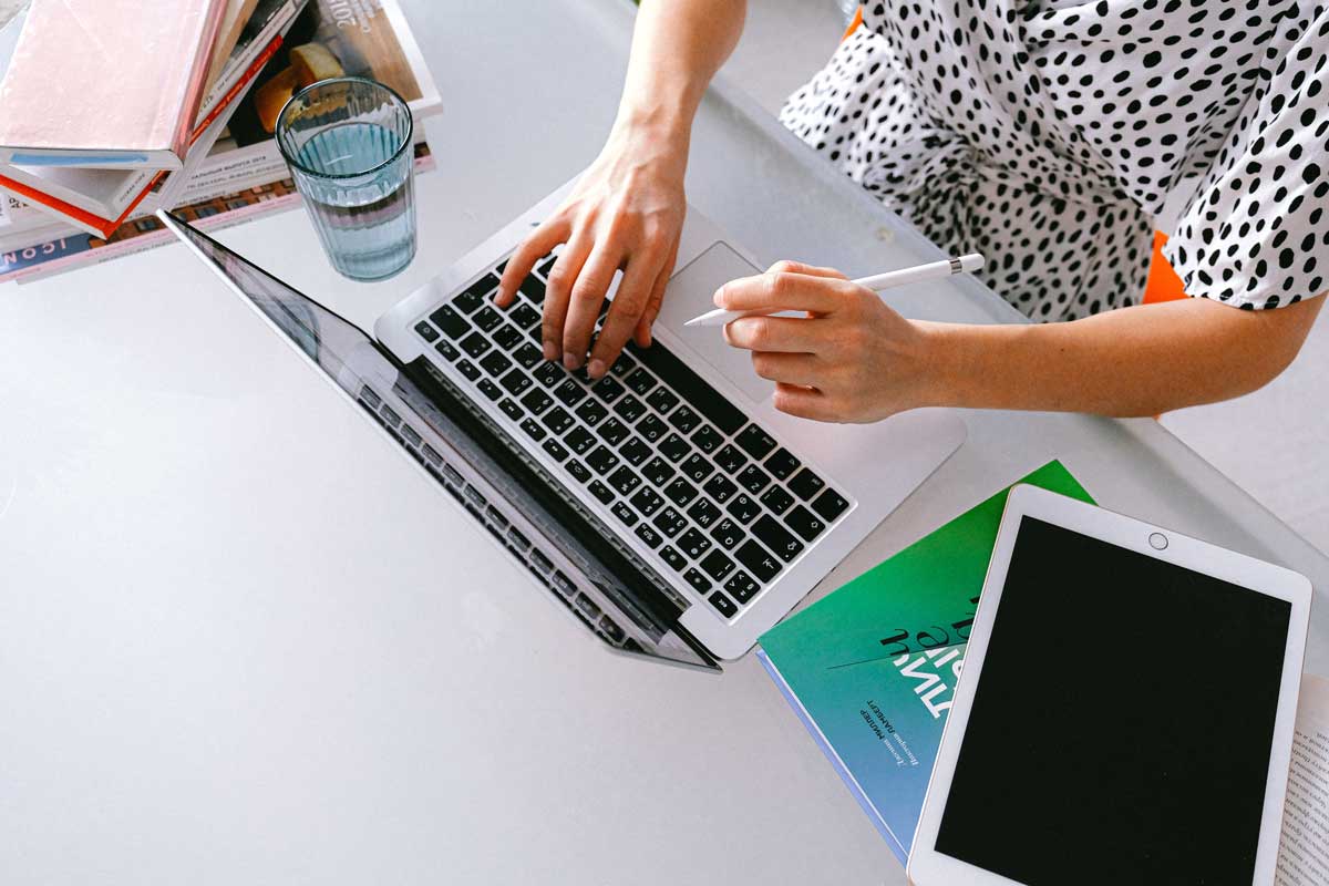 Overhead view of person working on laptop, with books and tablet close at hand.